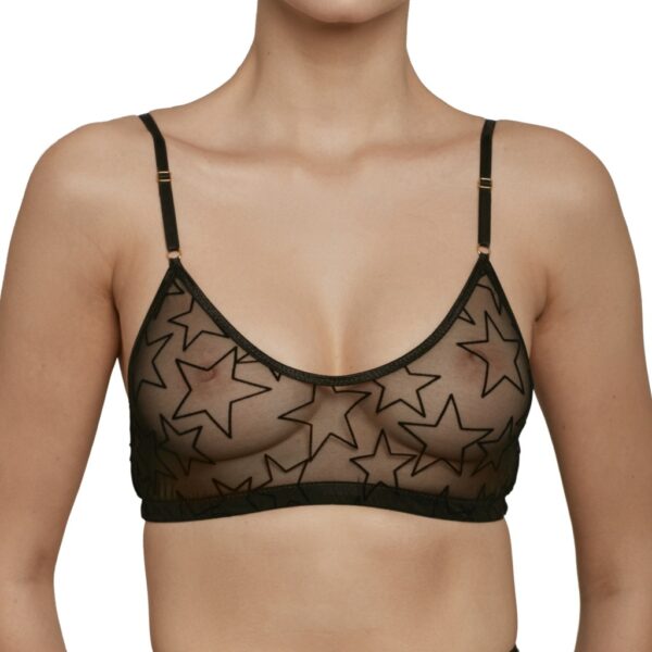 A model wears Le Petit Trou Audre bralette. The bra is black and sheer, with velvet stars outlined flocked onto the material. The bralette is a sporty style with no darts and a scoop neck.