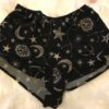 A flat lay of the Only Hearts Seeing Stars lounge shorts. The shorts are navy and feature a print of moons, stars and constellations printed in white and light pink. They are a loose fit but short inseam shorter than boxer shorts.