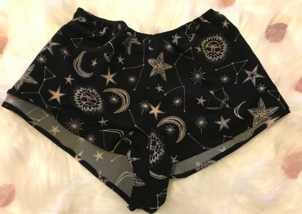 A flat lay of the Only Hearts Seeing Stars lounge shorts. The shorts are navy and feature a print of moons, stars and constellations printed in white and light pink. They are a loose fit but short inseam shorter than boxer shorts.
