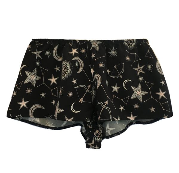 A flat lay of the Only Hearts Seeing Stars lounge shorts. The shorts are navy and feature a print of moons, stars and constellations printed in white and light pink. They are a loose fit but short inseam shorter than boxer shorts.