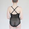 Model facing backwards and showing the back of the black mesh Iona bodysuit. It is sheer and features criss-crossed adjustable straps.