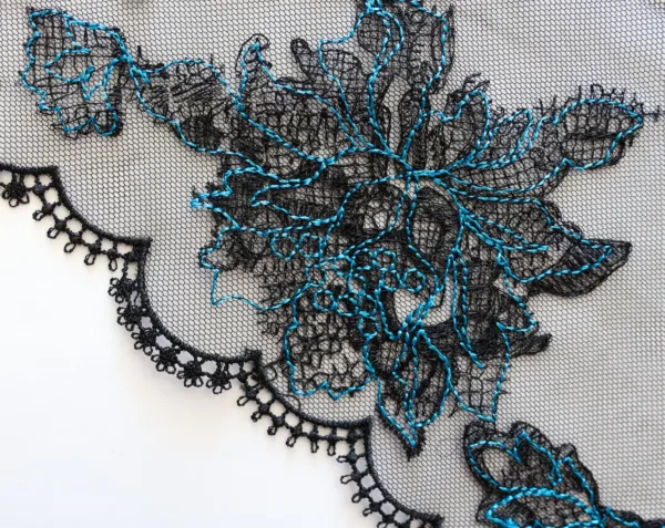 close up of the lace applique on kilo brava's halter neck mesh bodysuit in black and jewel-tone blue
