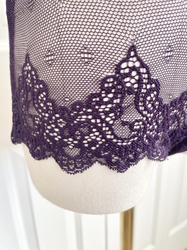 pictured on a dress form mannequin: close up of the bottom lace edge of the only hearts halter so fine lace bodysuit teddy in purple.