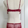 back view of a mannequin posed with red lingerie. the mannequin wears the only hearts so fine lace coucou peek-a-boo bralette and the matching coucou culotte brief. the mannequin is in front of a white door.