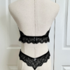 back view of a mannequin posed with black lingerie. mannequin wearing the only hearts so fine lace halter cami and matching lace thong panty. the mannequin is standing in front of a white door.