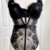 front view of a mannequin wearing the kilo brava black embroidered lace underwire bodysuit. the mannequin is in front of white doors.
