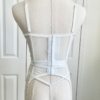 back view of a mannequin wearing lingerie in front of white doors. mannequin wears the kilo brava floral embroidered underwire bustier, garter belt, and g-string panty.