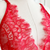 close in view of the bust area of a mannequin wearing red lingerie - the kilo brava eyelash lace teddy in red - stands in front of white doors.