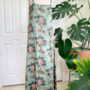 back view of a mannequin wearing the only hearts luv island night dress in moss green with a tropical print. The mannequin stands in front of a tropical plant and white doors.