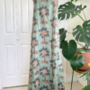 front view of a mannequin wearing the only hearts luv island night dress in moss green with a tropical print. The mannequin stands in front of a tropical plant and white doors.