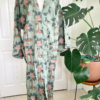 a mannequin wears the only hearts luv island kaftan in moss green with a tropical print. The mannequin stands in front of a tropical plant and white doors.