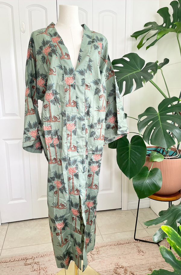 a mannequin wears the only hearts luv island kaftan in moss green with a tropical print. The mannequin stands in front of a tropical plant and white doors.