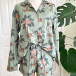 a mannequin wears the only hearts luv island shorty pj set in moss green with a tropical print. The mannequin stands in front of a tropical plant and white wall.