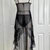back view of a mannequin dressed with the only hearts coucou lola moonchild dress. It's a sheer black lingerie slip dress with a polka dot pattern, three ties at the bust, center front, and waist, and long ruffled skirt. Under the dress the mannequin has on sheer black underwear in the same dotted pattern.
