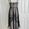 back view of a mannequin dressed with the only hearts coucou lola moonchild dress. It's a sheer black lingerie slip dress with a polka dot pattern, three ties at the bust, center front, and waist, and long ruffled skirt.