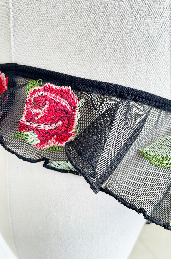 close up of a Mannequin wearing black sheer lingerie with rose embroidery and ruffled edges, the only hearts A Rose is A Rose butterfly brief, set against a white background.