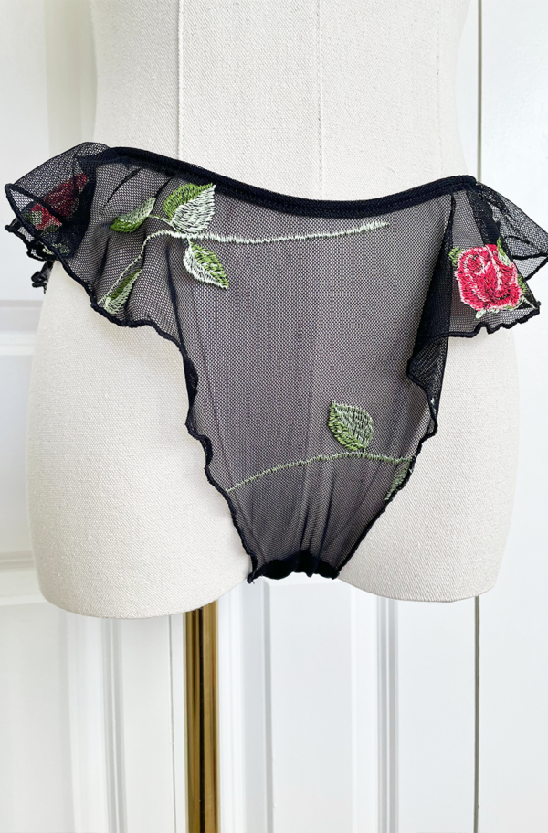 Mannequin wearing black sheer lingerie with rose embroidery and ruffled edges, the only hearts A Rose is A Rose butterfly brief, set against a white background.