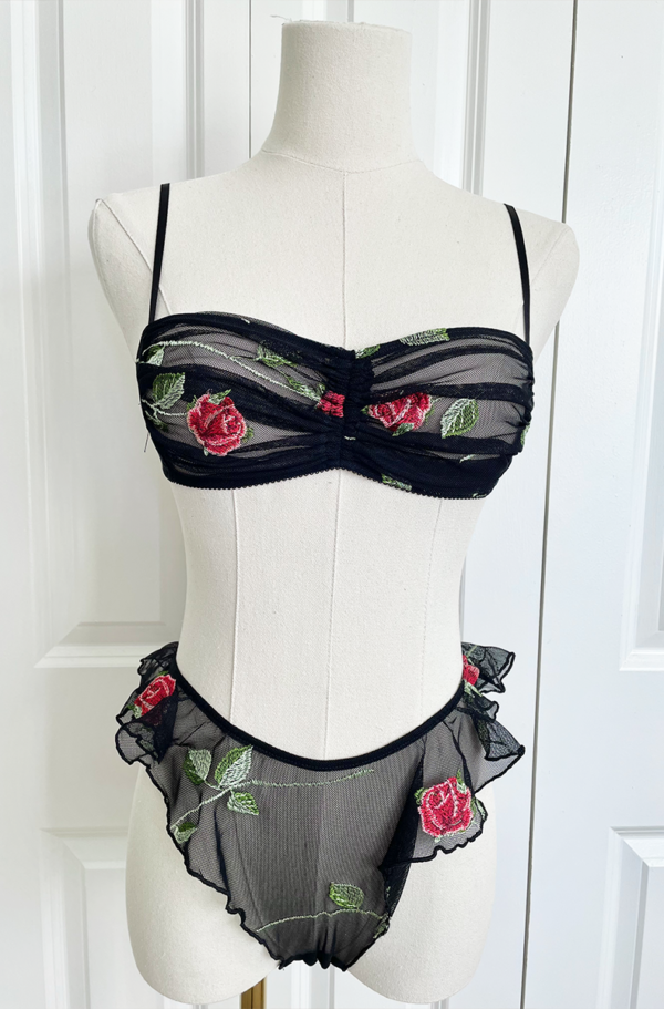 Mannequin wearing black sheer lingerie with rose embroidery and ruffled edges, the only hearts A Rose is A Rose bra and underwear set, set against a white background.