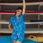 Model wearing Cotton Shortie PJ Set in Resort Palms, a tropical blue palm print pajama set with a short-sleeve button-down top and matching shorts.